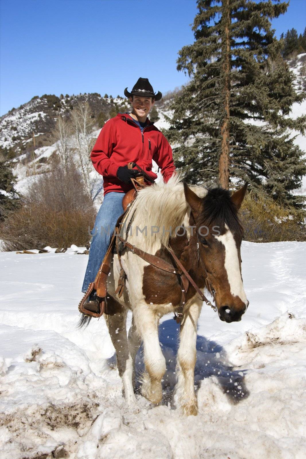 Young Caucasian man horseback riding in snowy mountains looking at viewer.