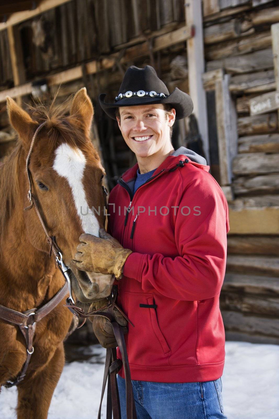 Young adult Caucasian male in cowboy hat petting horse.