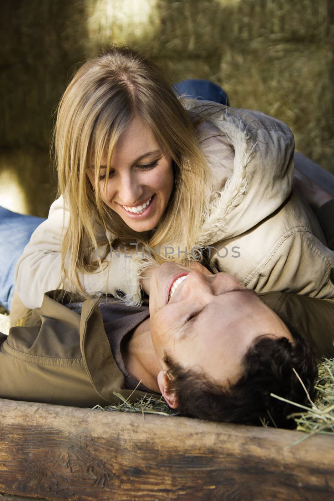 Young adult Caucasian couple lying in hay.