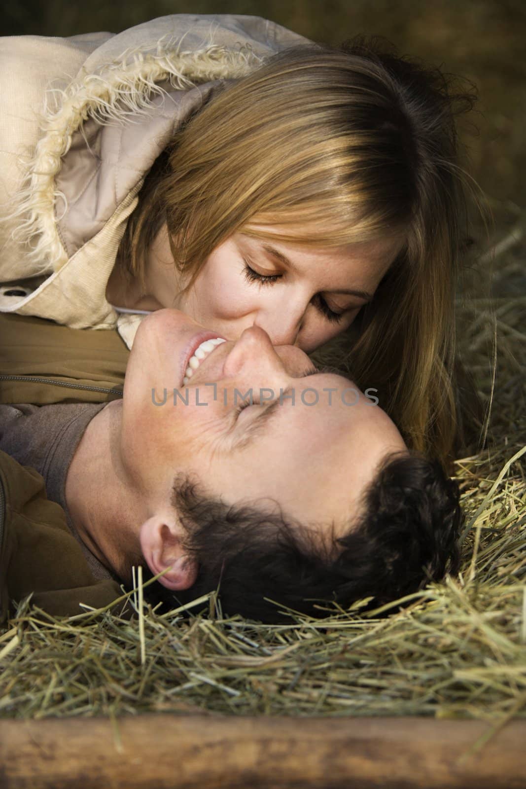 Young adult Caucasian woman kissing boyfriend while lying in hay.