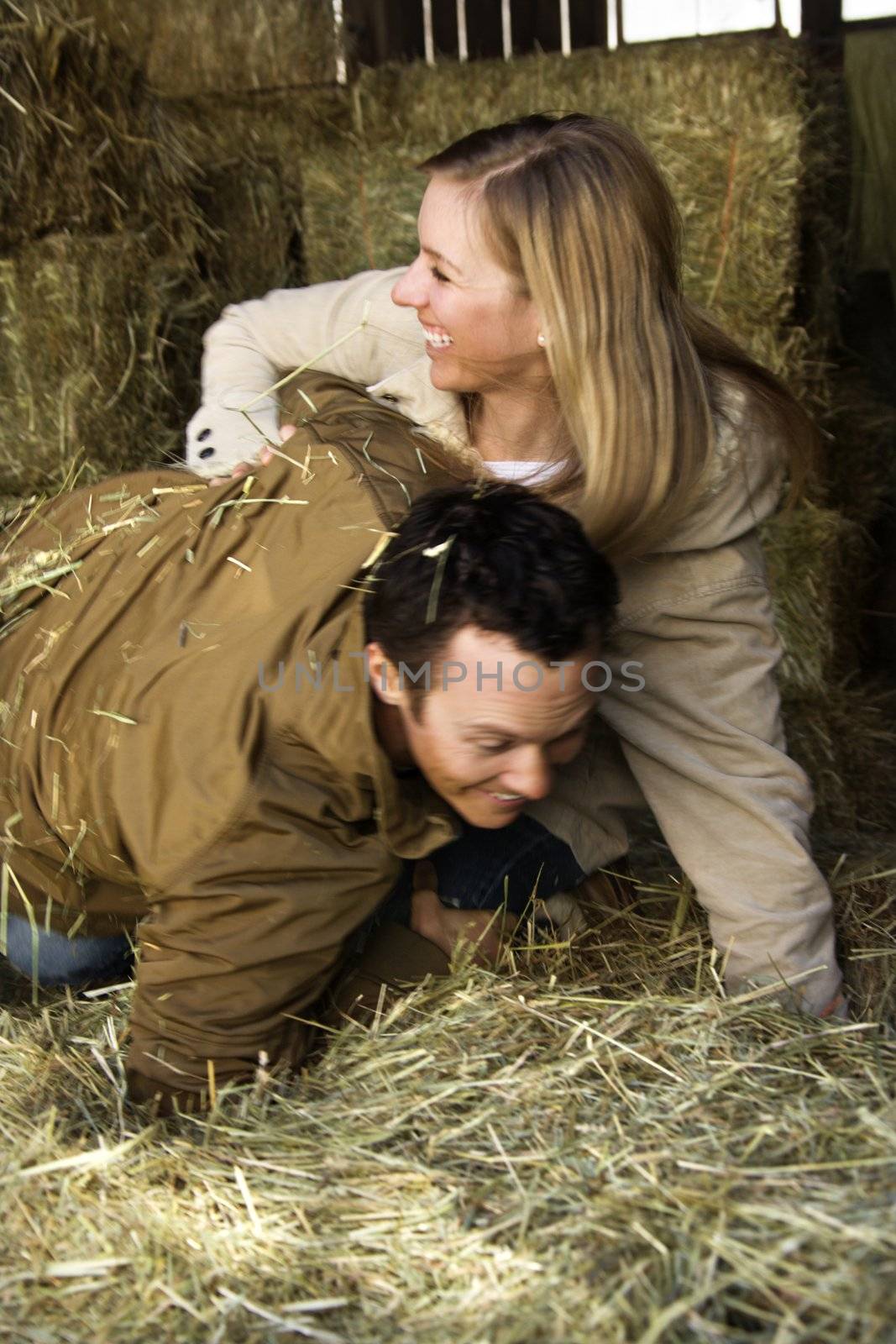 Young adult Caucasian couple playing in hay.