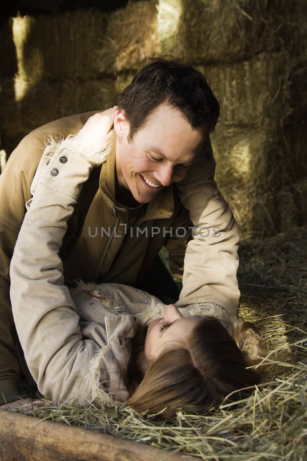 Young adult Caucasian couple laying in hay embracing.