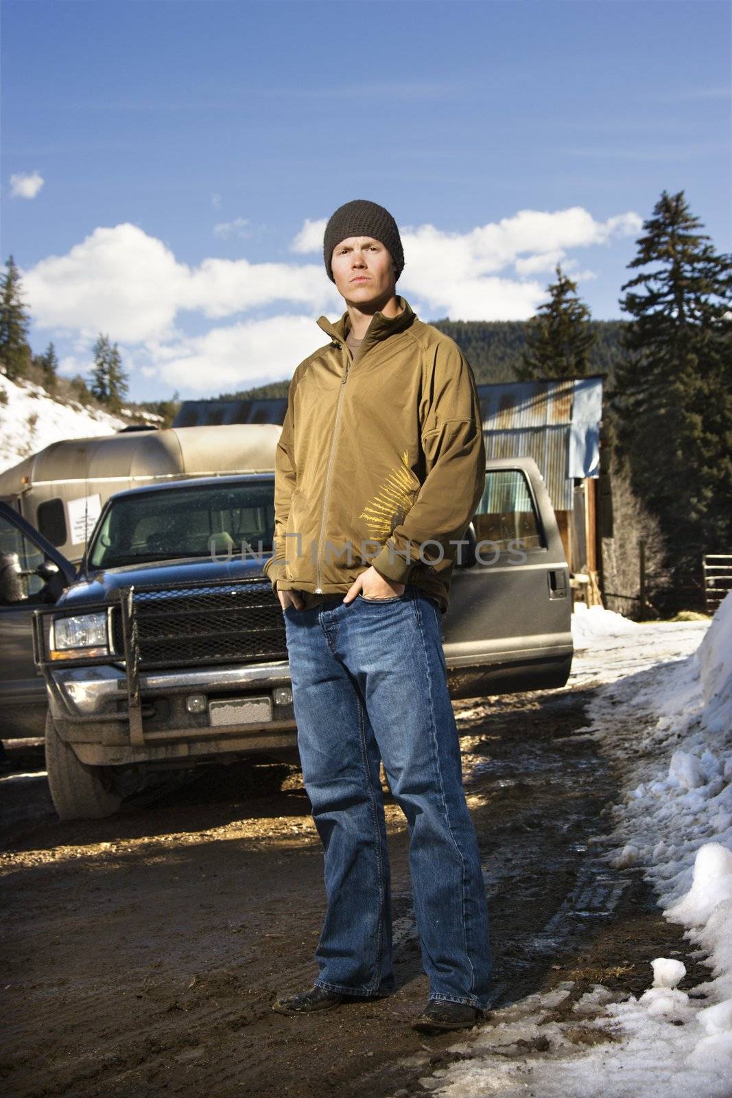 Young Caucasian man standing in front of truck with hands in pockets looking at viewer.