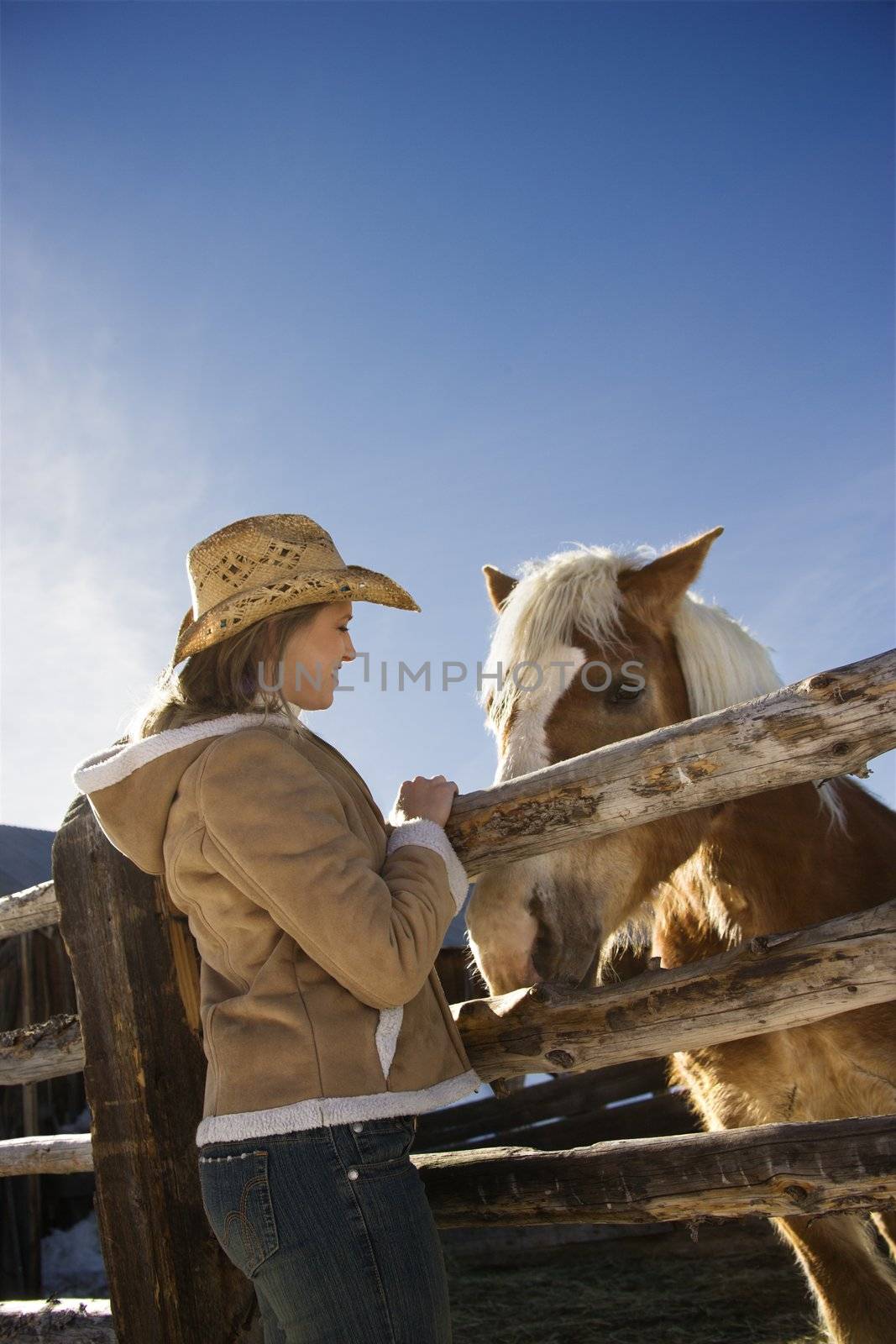 Young Caucasian woman standing at fence with horse.