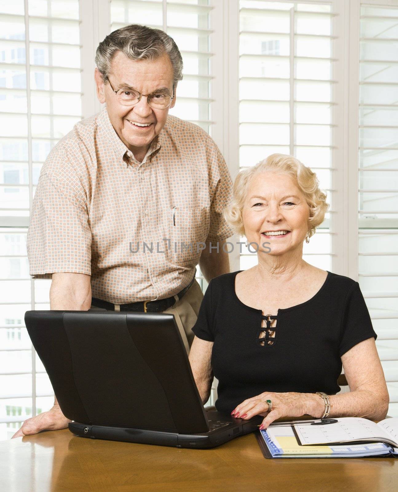 Mature Caucasian couple looking at their calendar and using laptop.