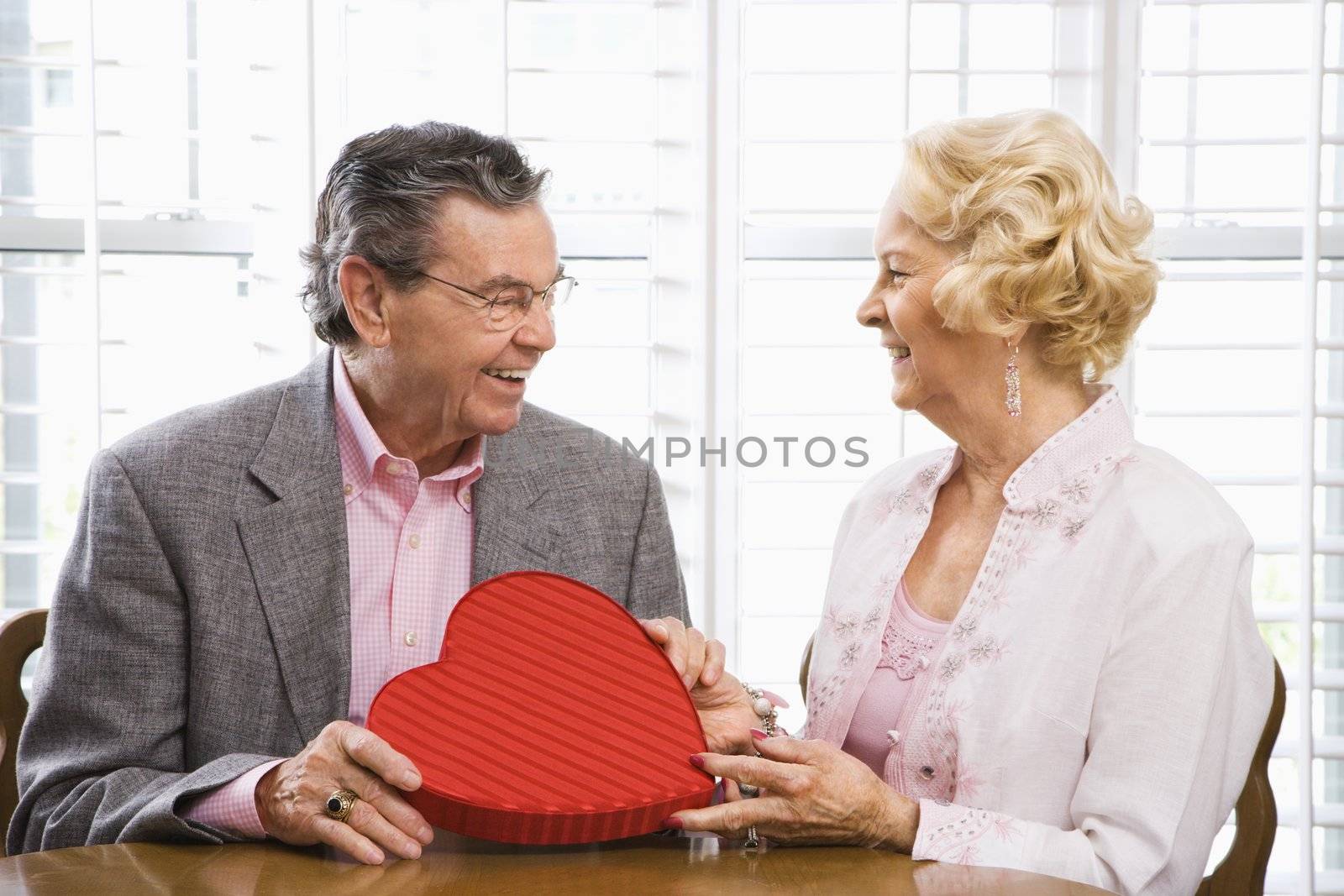 Mature Caucasian man giving Valentine heart box to mature Caucasian woman.