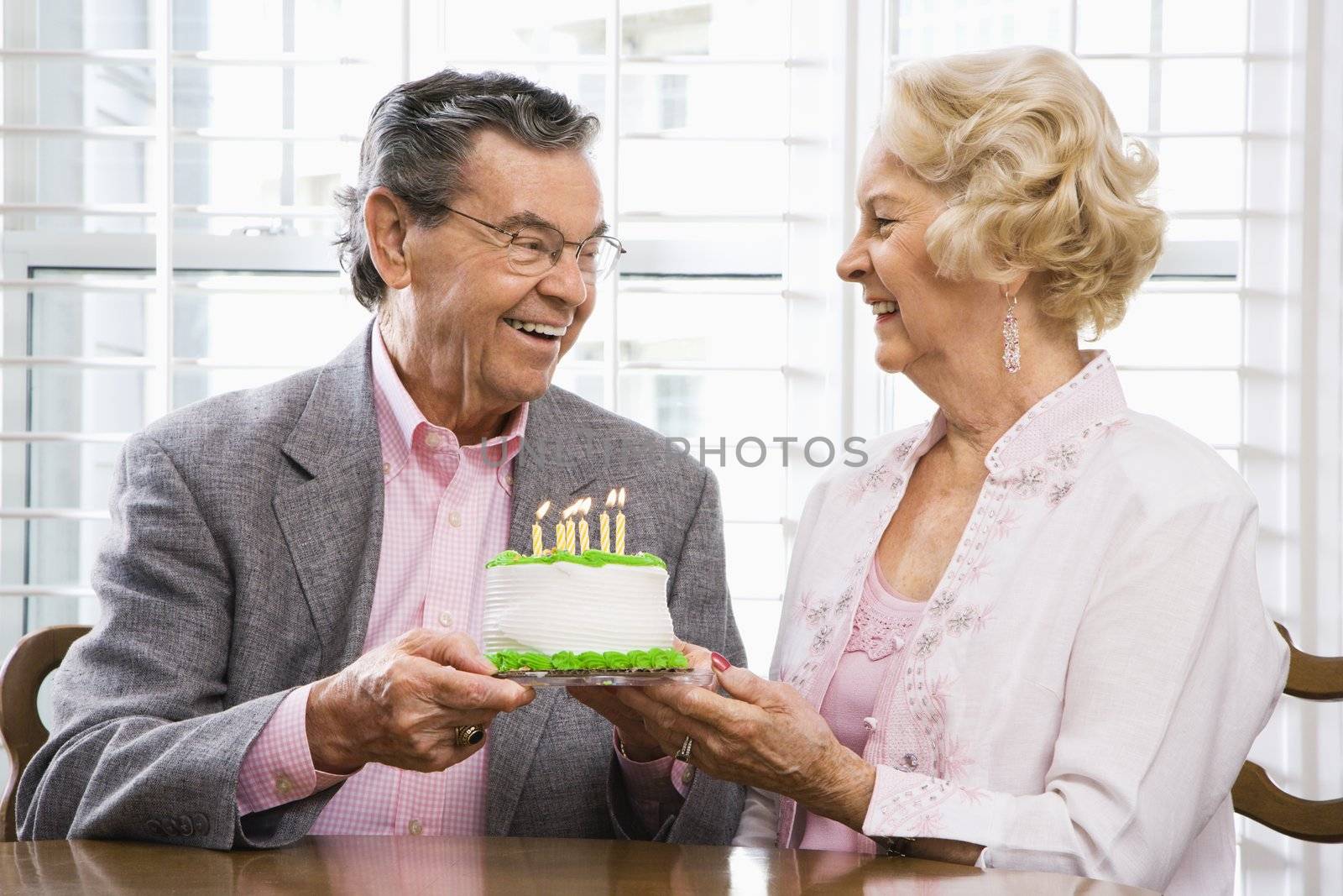 Mature Caucasian couple holding birthday cake looking at each other.