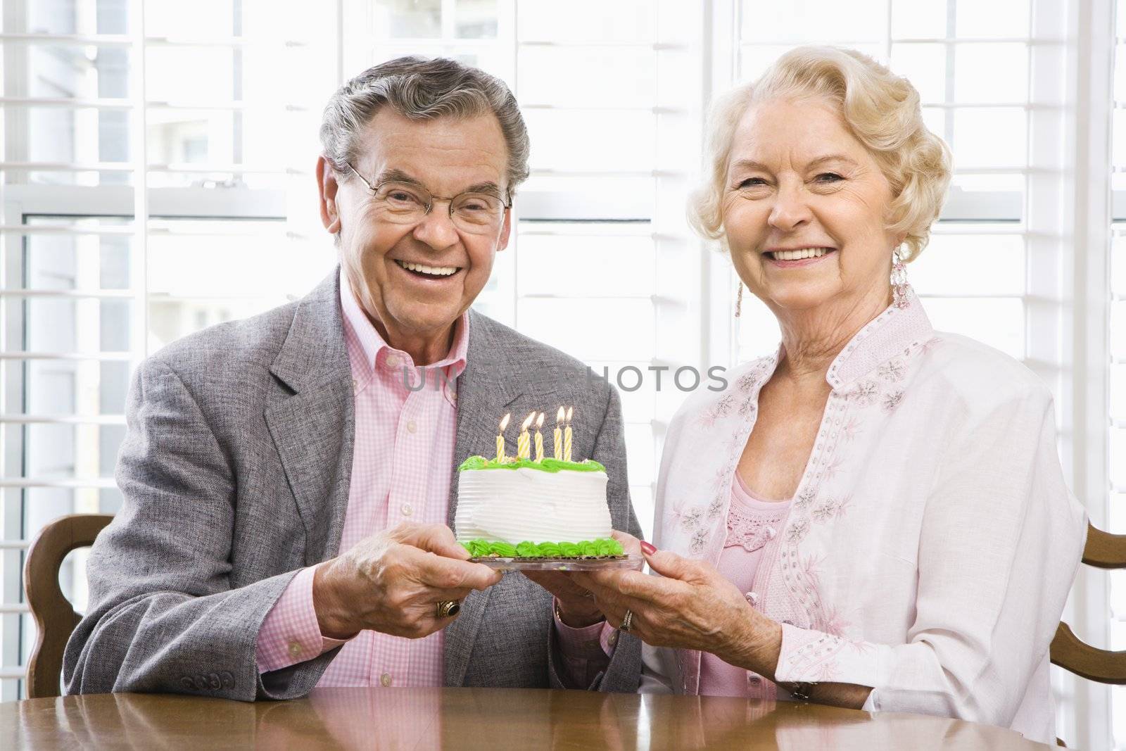 Mature Caucasian couple holding birthday cake looking at viewer.