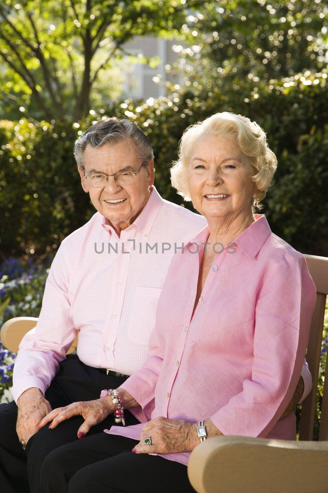 Mature Caucasian couple sitting on bench looking at viewer.