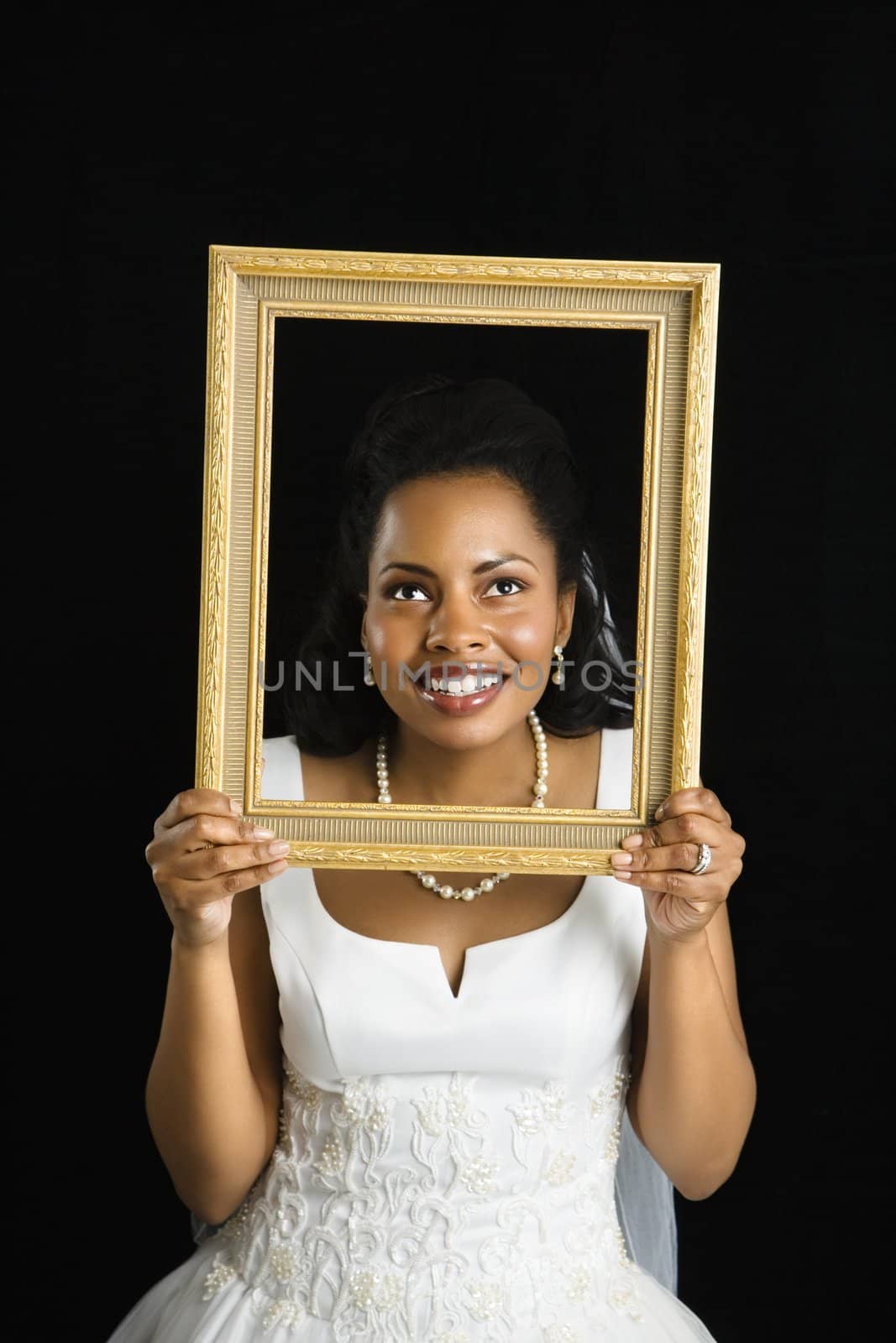 Mid-adult African-American bride holding frame around her face.