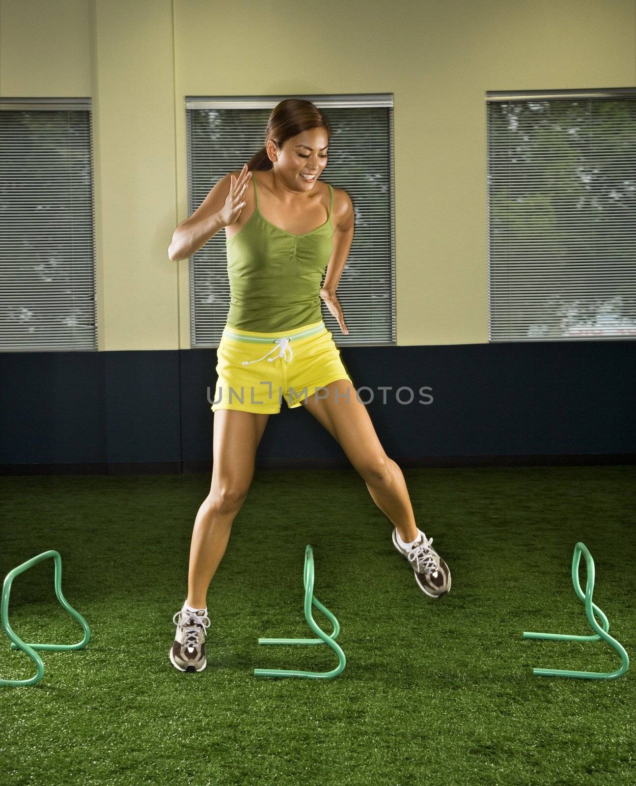 Asian female jumping over hurdles sideways inside.