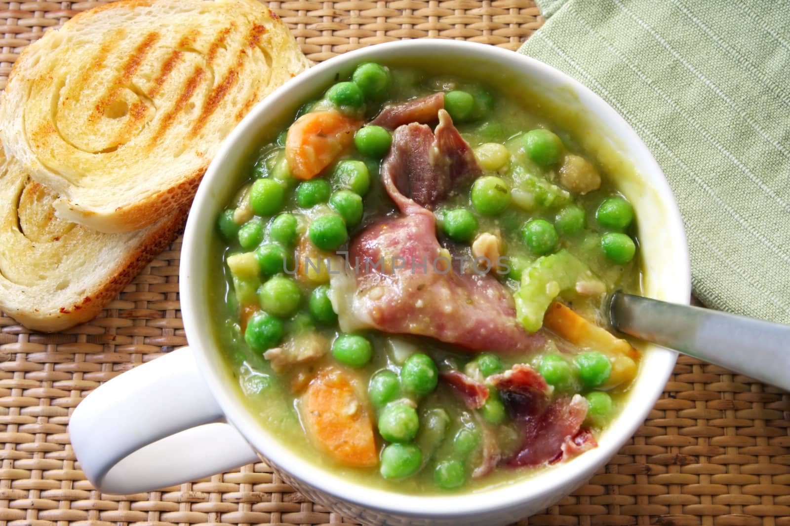 A cup of hearty pea and ham soup with crusty sourdough bread.  The ham is crispy prosciutto.