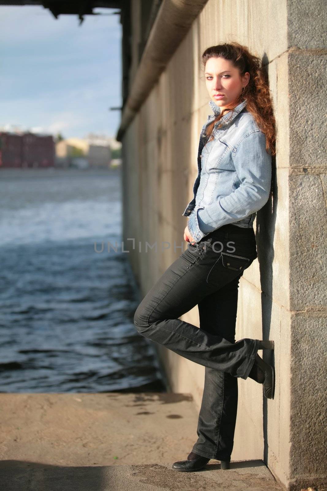 portrait of the beautiful brunette in jeans jacket near stone wall, river