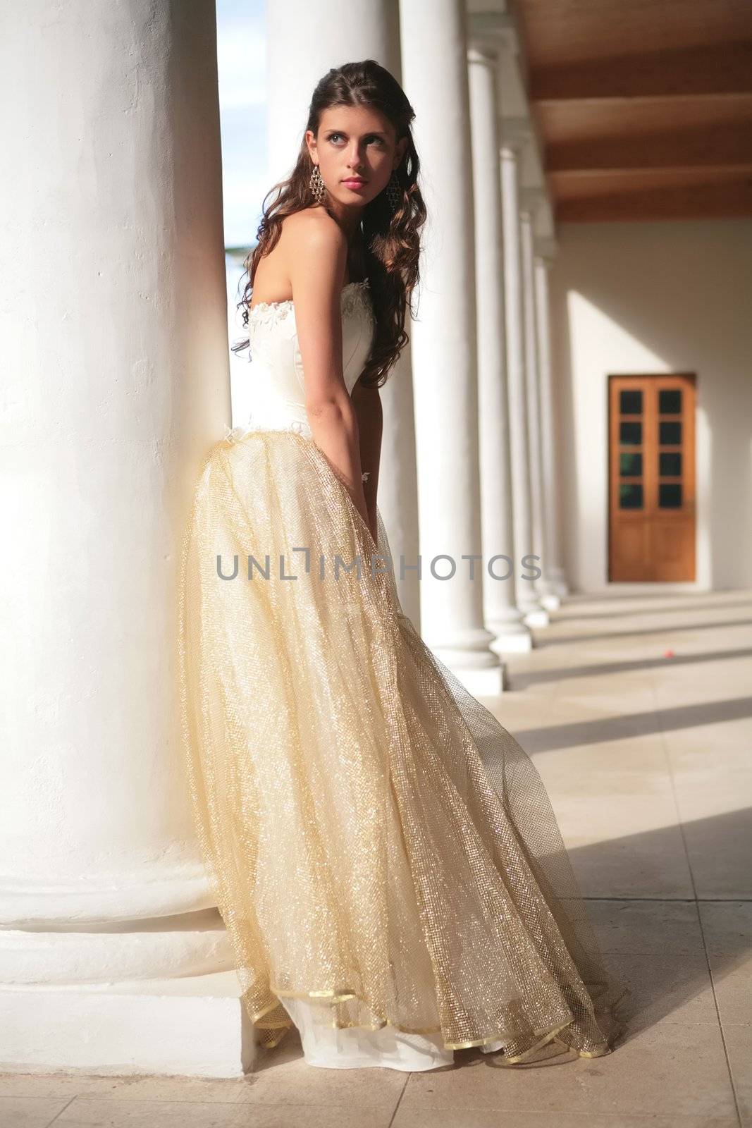 girl in white-golden gown of the bride amongst colonnades of the old-time building