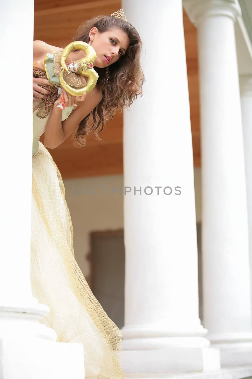 beautiful girl in gown of the bride with doll peers out from behind pillar