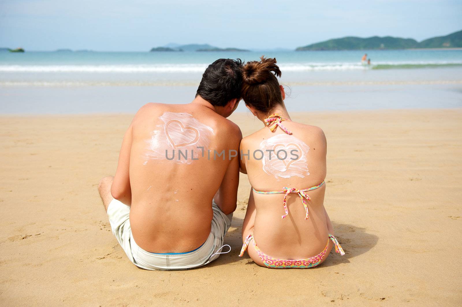 Young couple enjoying the beach with an heart draw on their backs