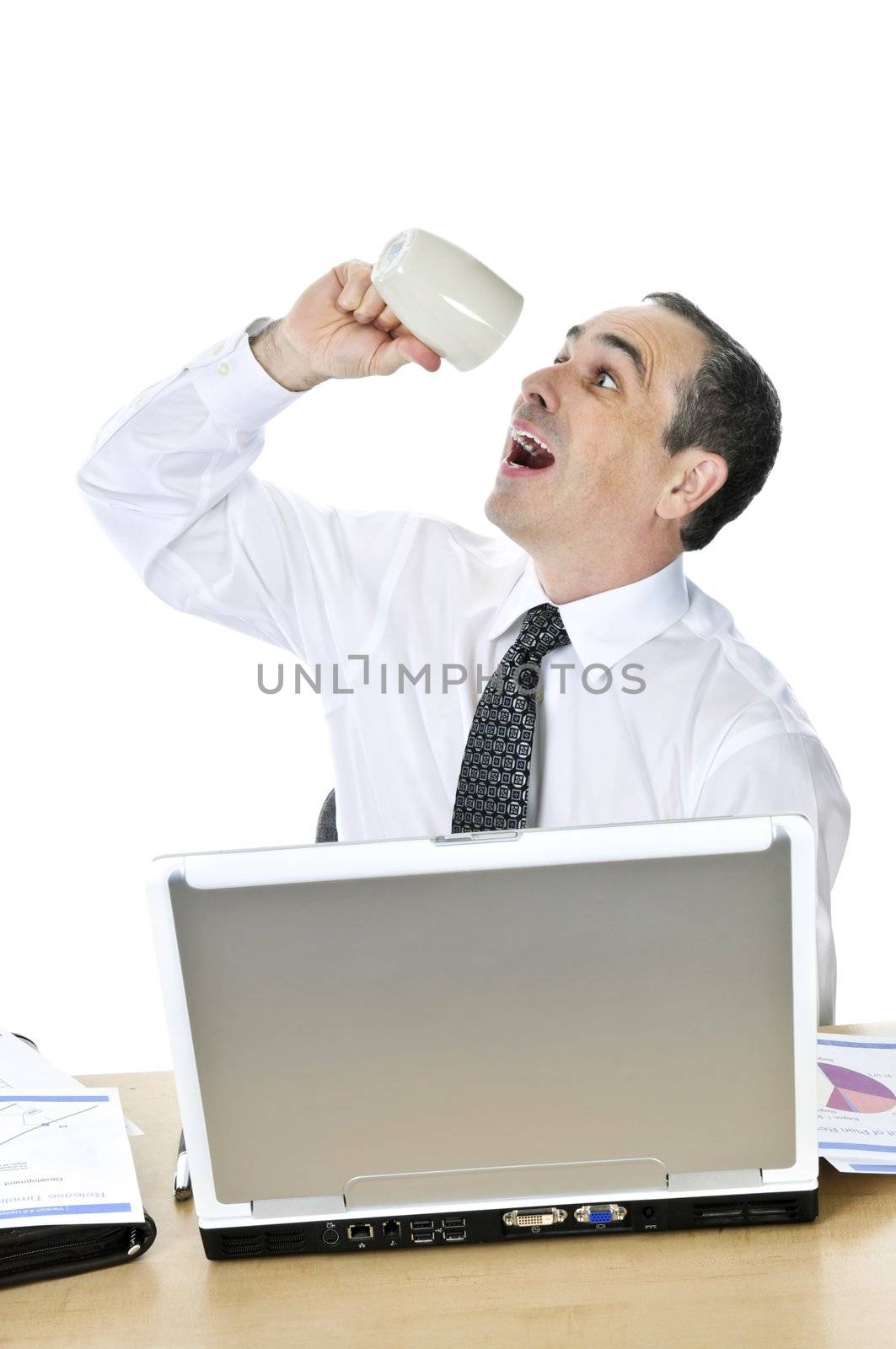 Overworked businessman with coffee mug at his desk isolated on white background