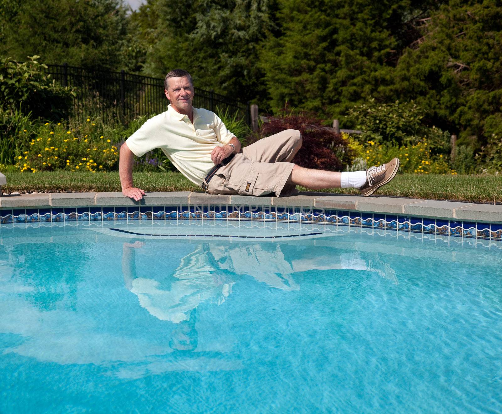 Middle aged man relaxes by the side of a pool in a flowery backyard garden