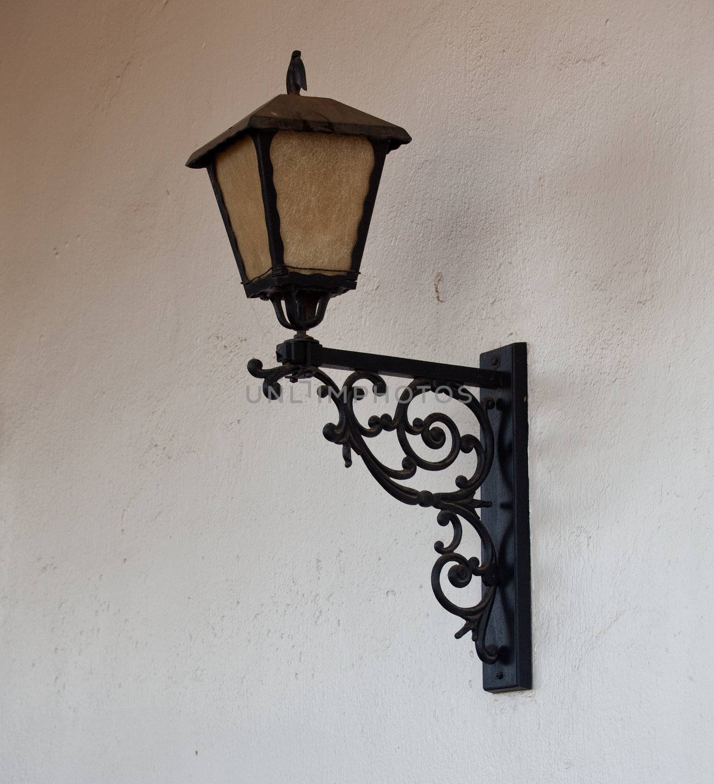 Black lacquered ornate lantern against a stucco wall of a mission in California