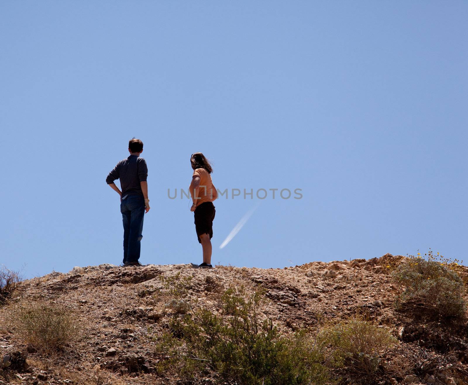 Hikers in desert point to aircraft trail by steheap