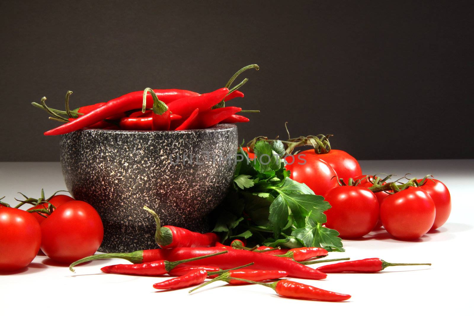 Red peppers and tomatoes with granite bowl on dark background