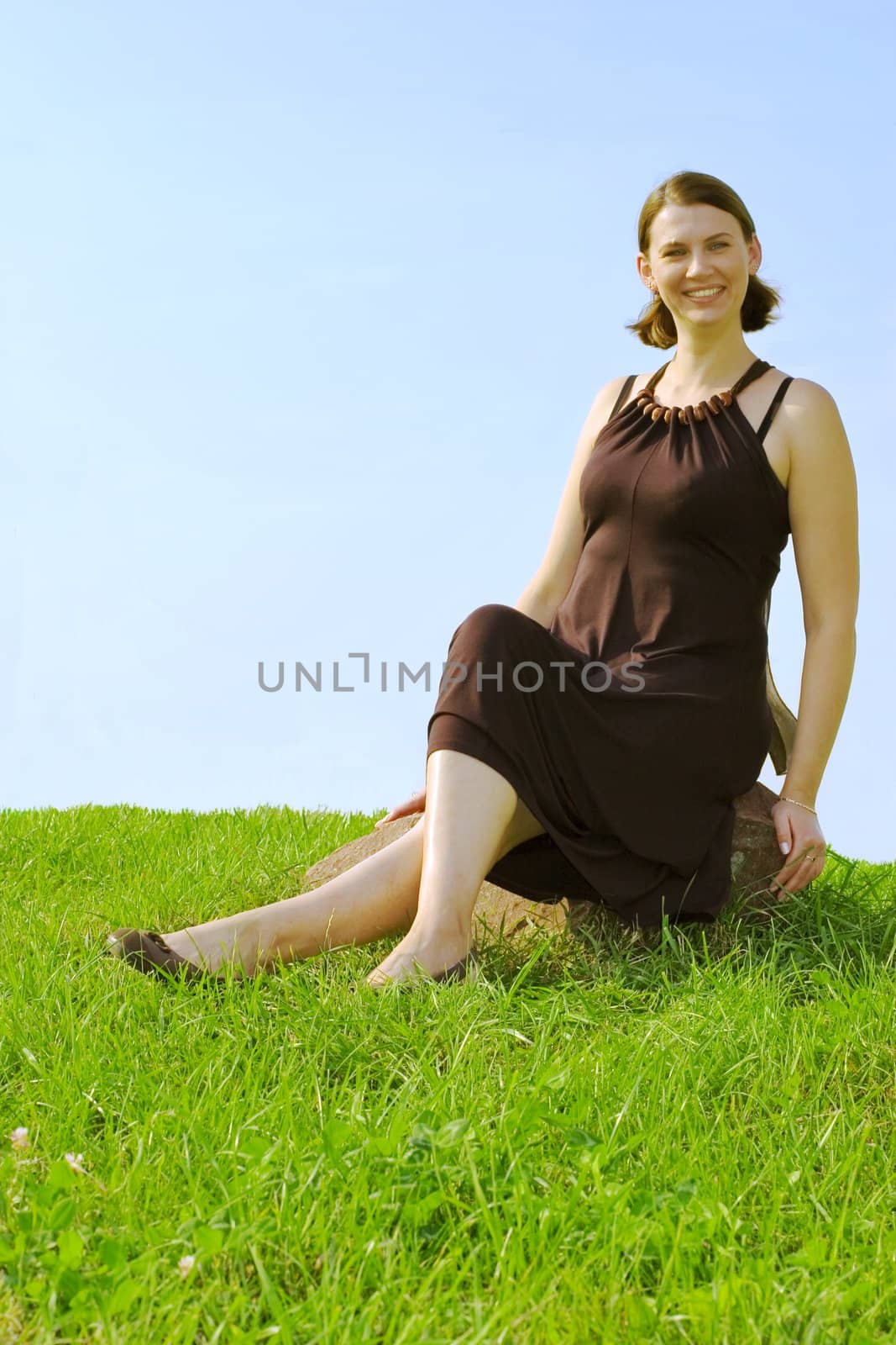 Smiling girl sitting on stone on blue sky