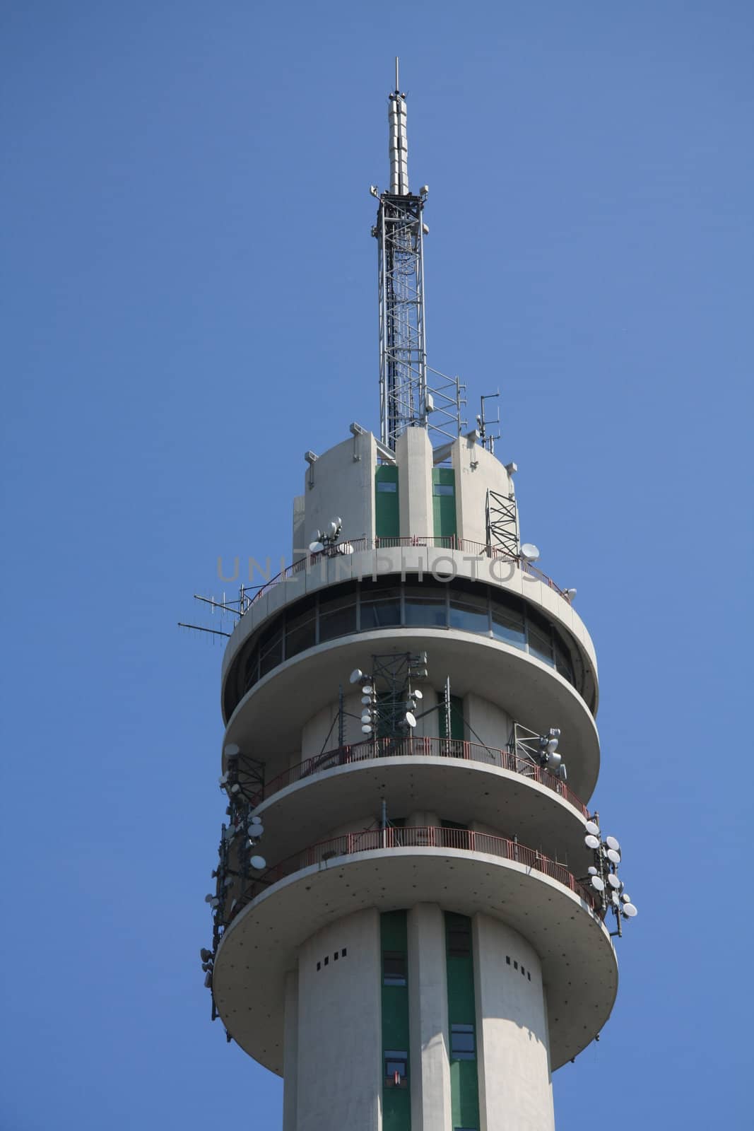 A telecommunication tower in a clear blue sky, showing loads of antennas and satelite connections