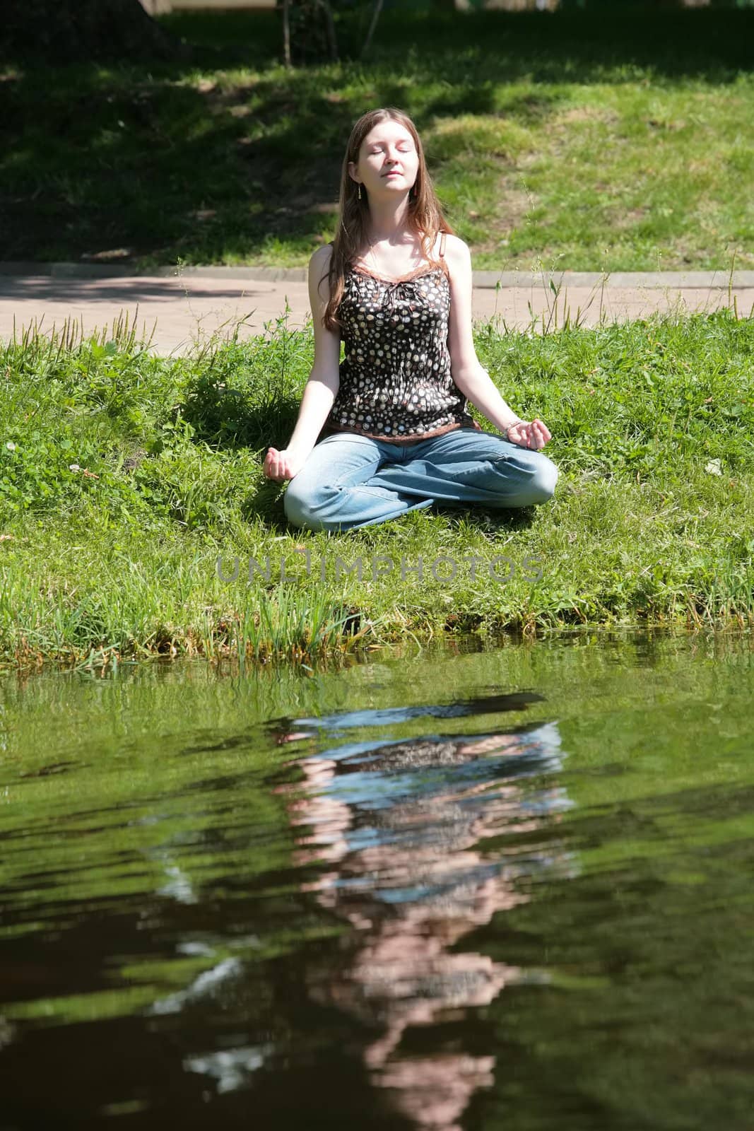 beautiful girl  in blue jeans meditating near by water