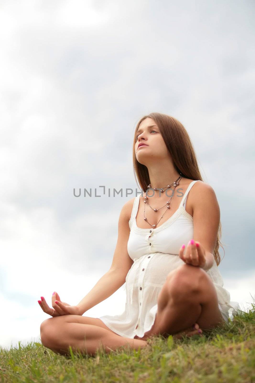 pregnant young woman sits on herb and meditating under opened sky