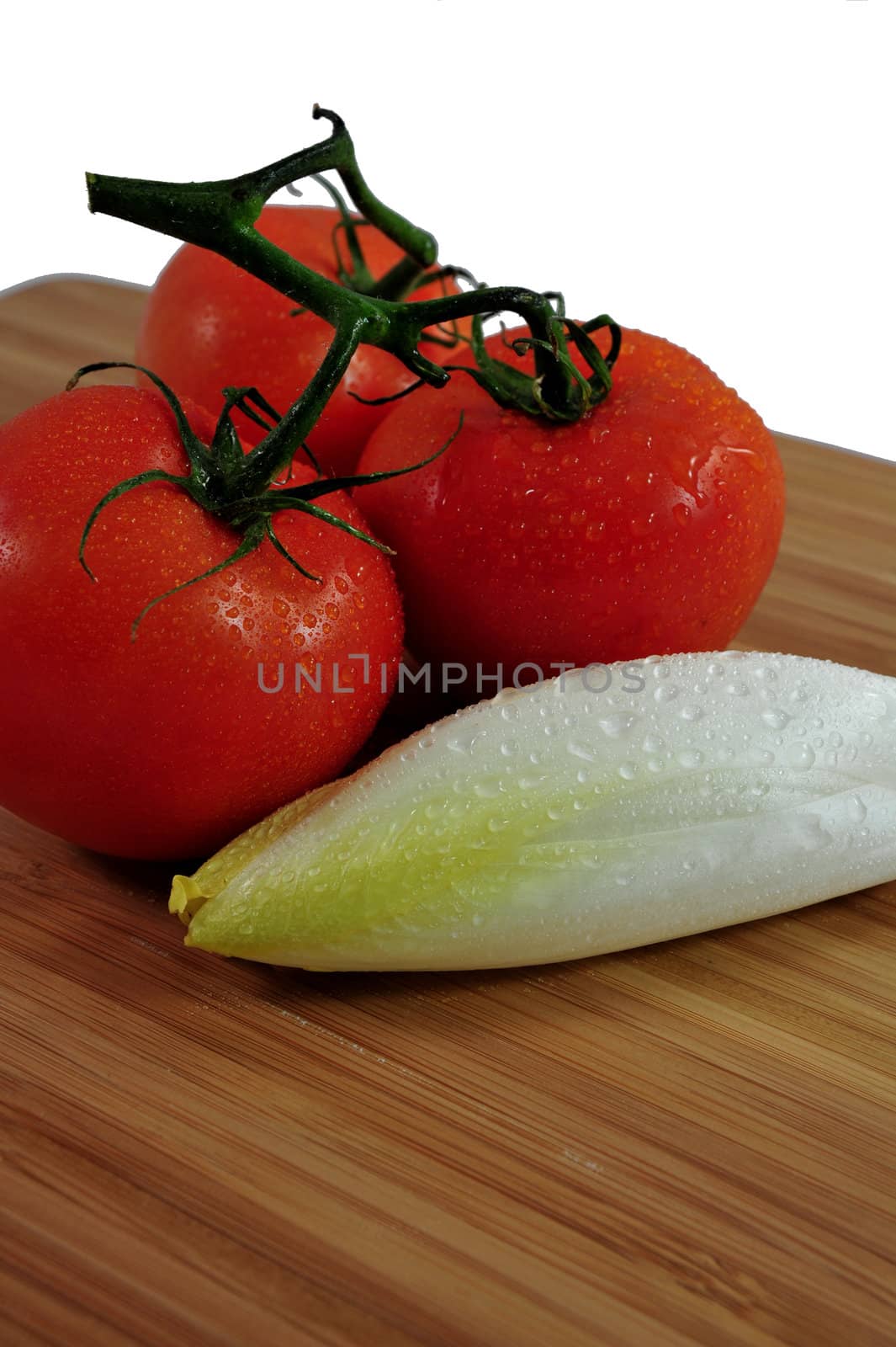 Thre tomatoes and Endive on a wooden cutting board.