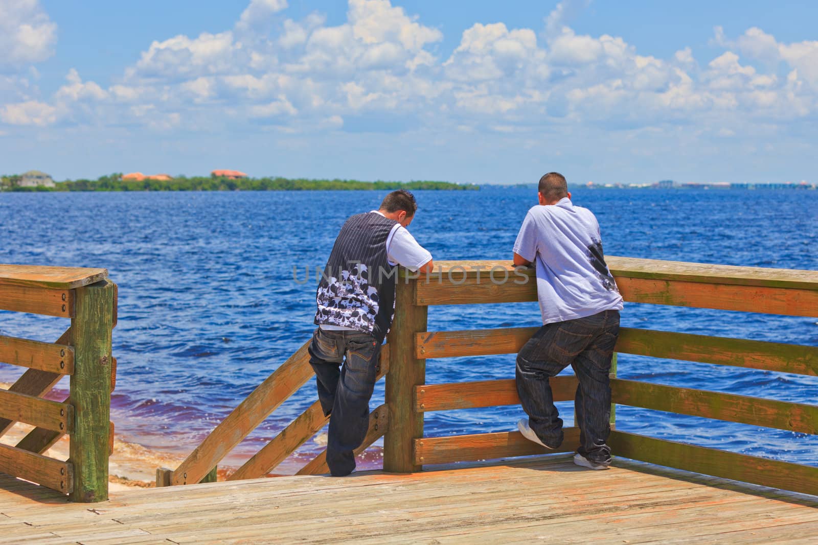 Two Hispanic men at the ocean standing on a pier looking out at the sea