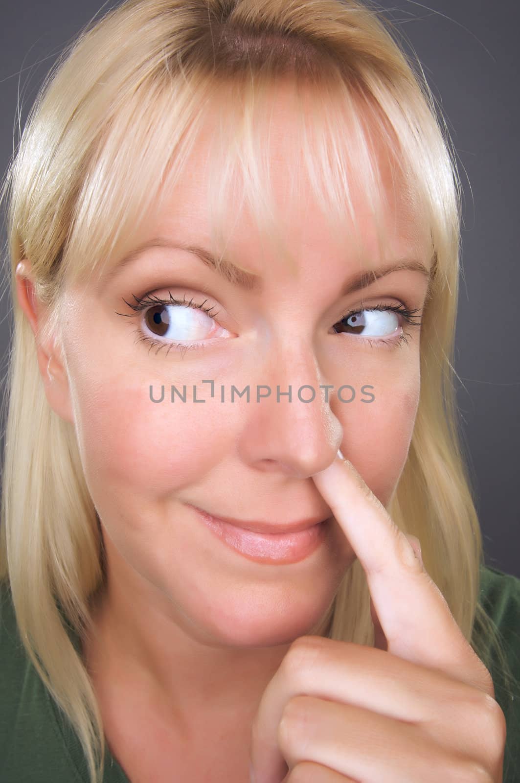 Blond Woman with Finger in Her Nose Against a Grey Background.