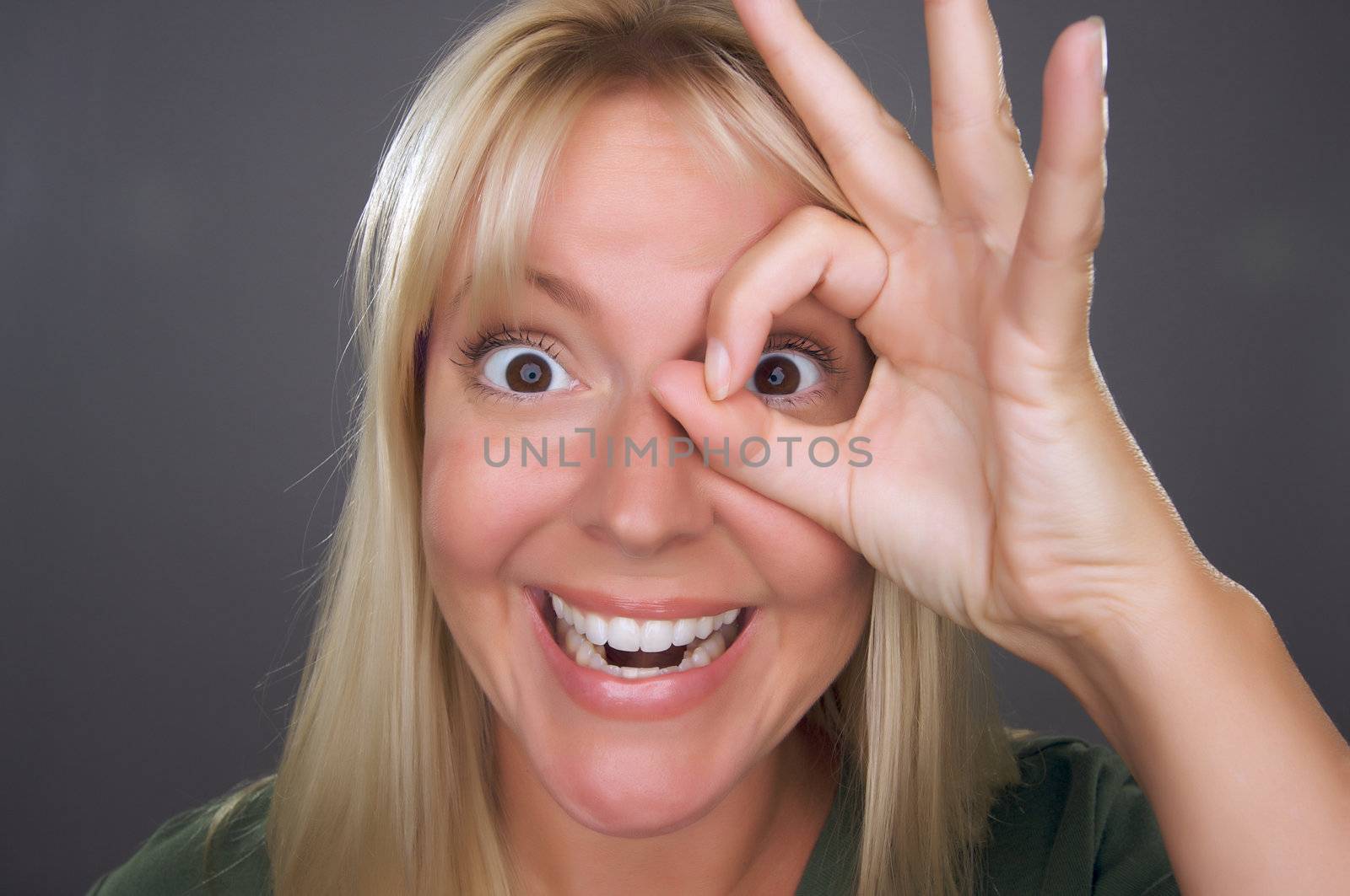 Woman with Okay Sign in Front of Face Against a Grey Background.