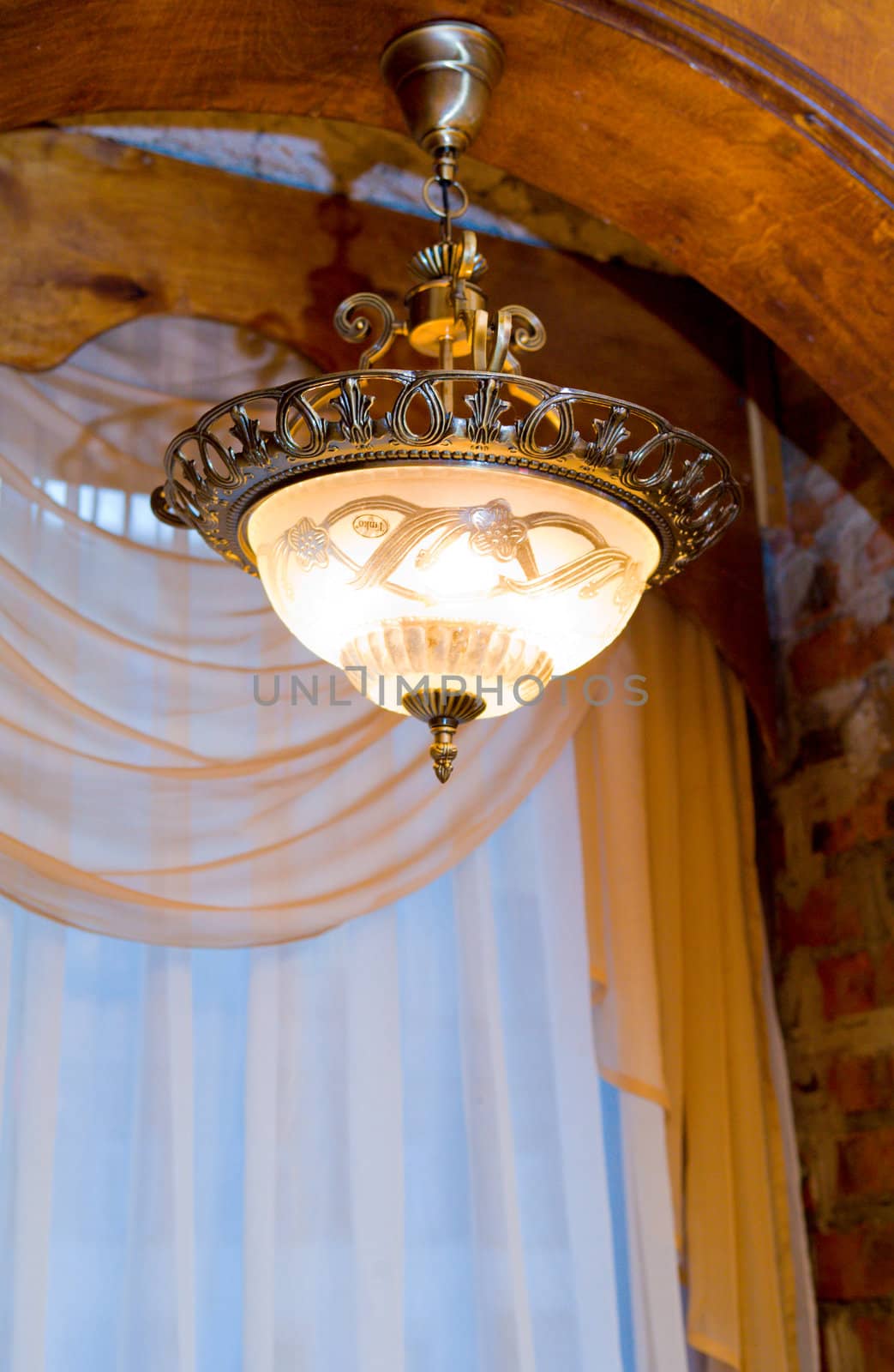 Old copper lamp under ceiling near window