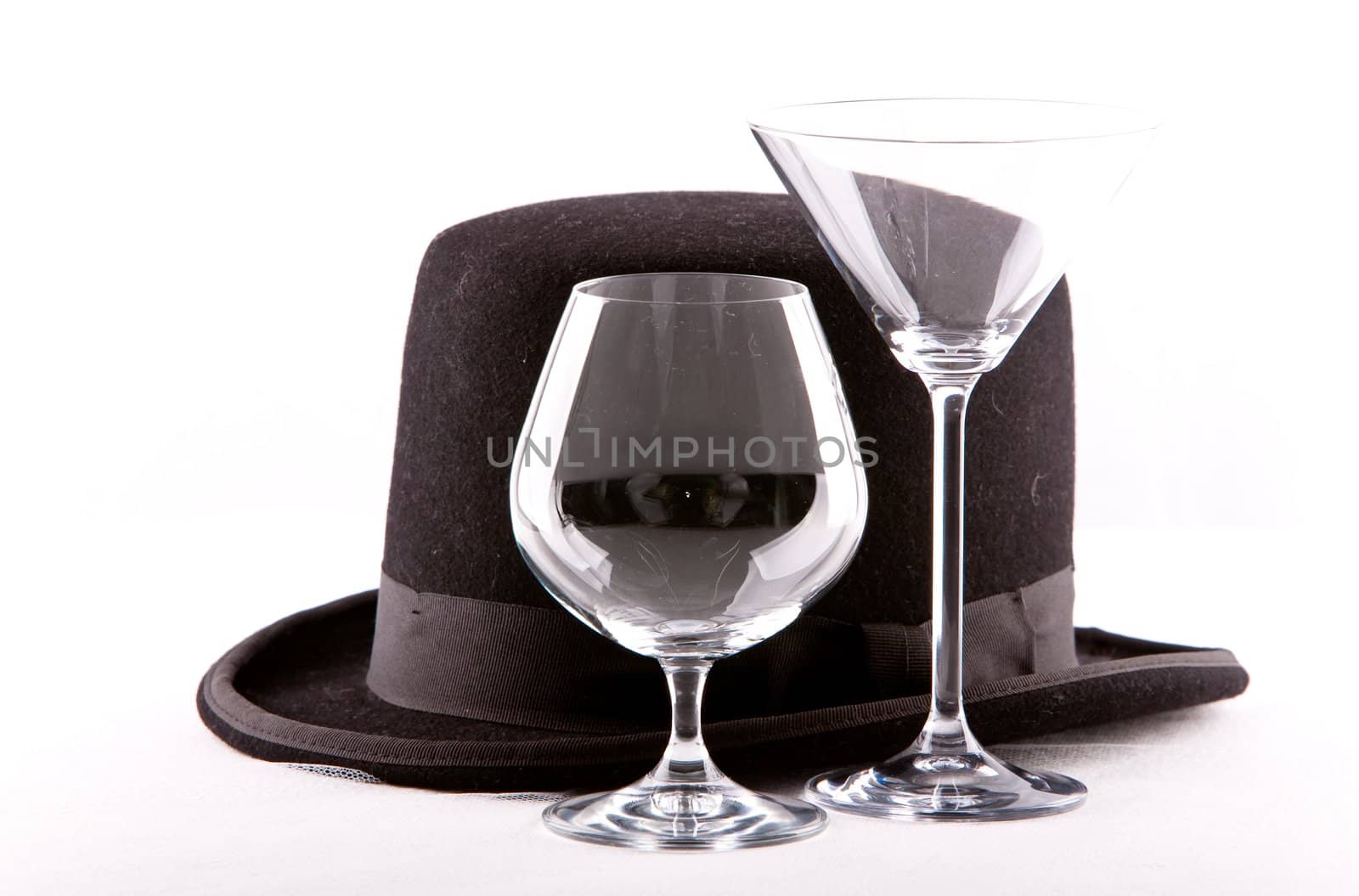 two empty wine martini or cognac glasses standing empty next to a top hat on a white background