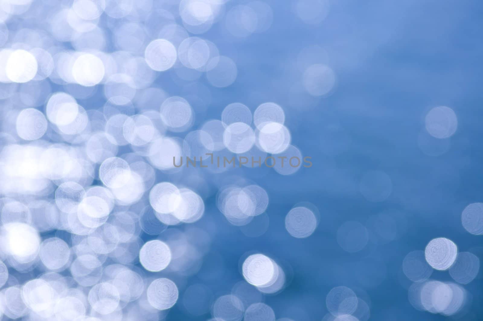 Out of focus bokeh background of blue water with sun reflections