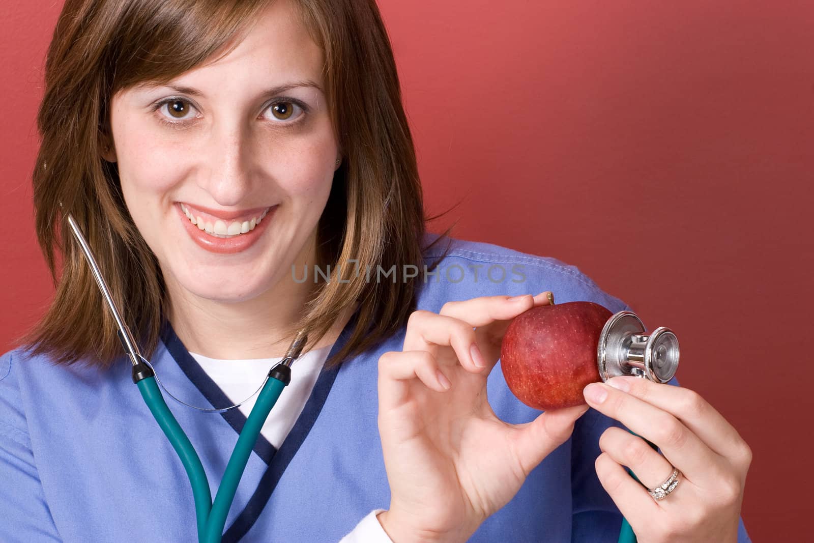 A young nurse is holding her stethoscope onto a red apple.  An apple a day keeps the doctor away.