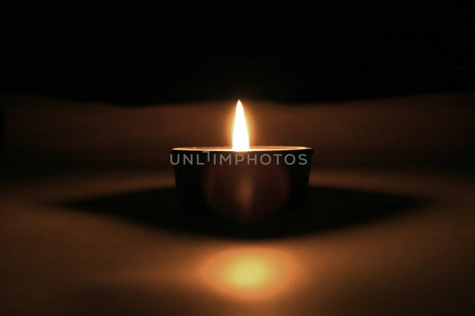 Solitary candle with reflections in the darkness