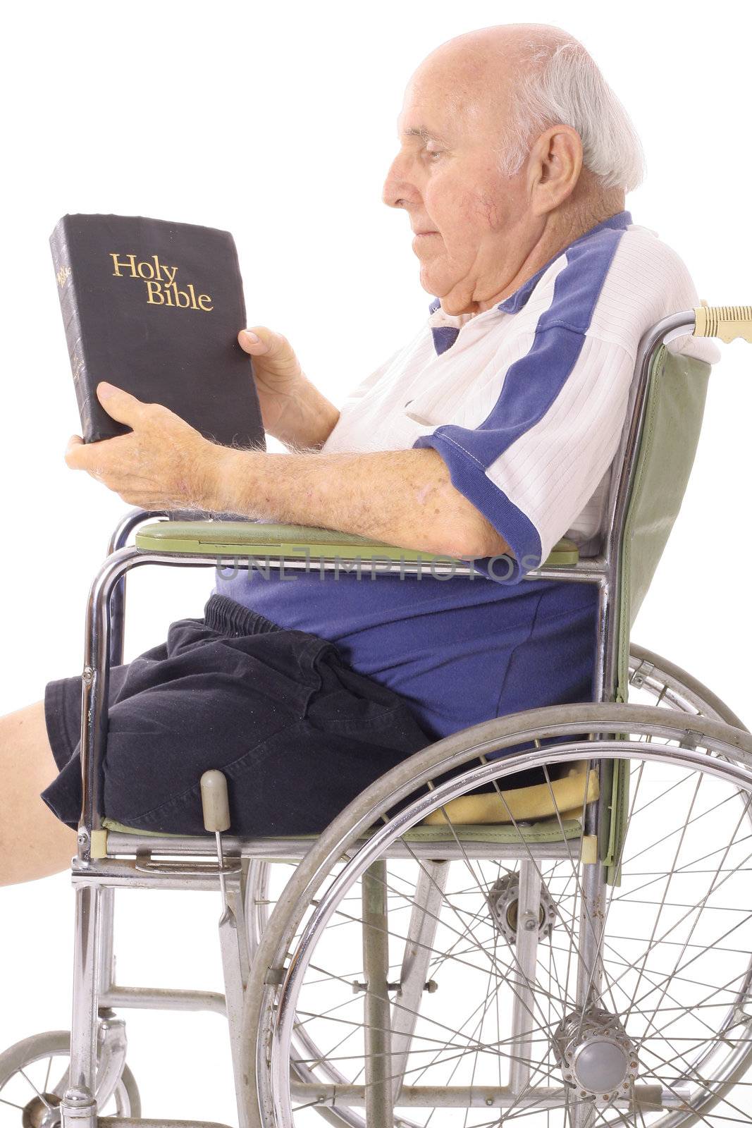 shot of an old man in wheelchair reading a bible by creativestock