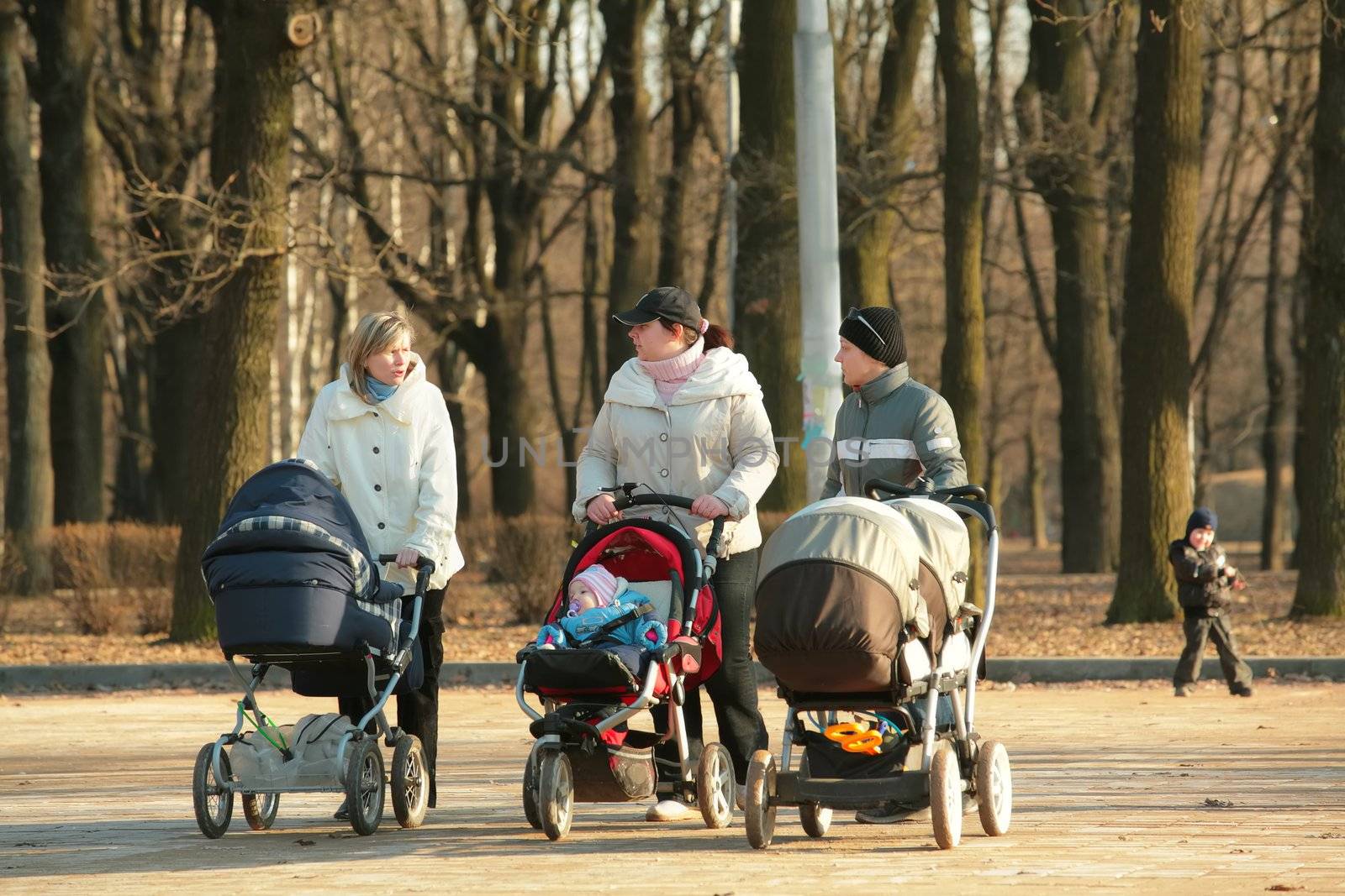 Three young mothers with sidercar on walk in spring park, editorial use only