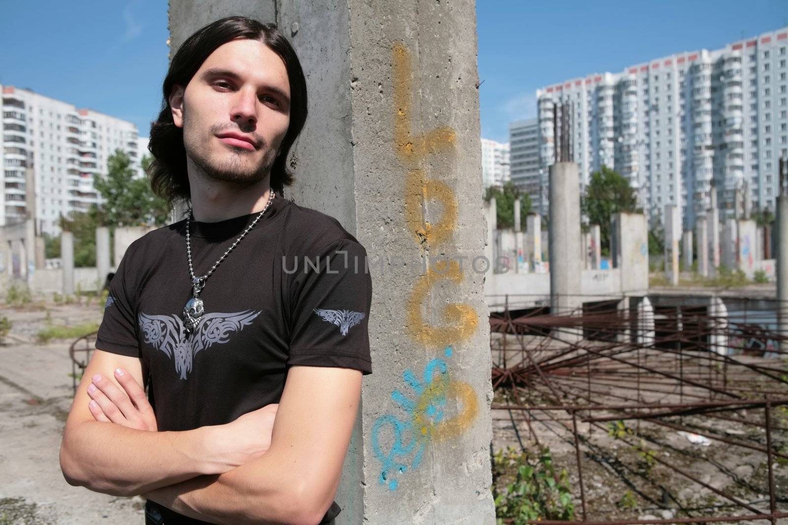 young man in black t-shirt with silver skull on chain on background concrete construction