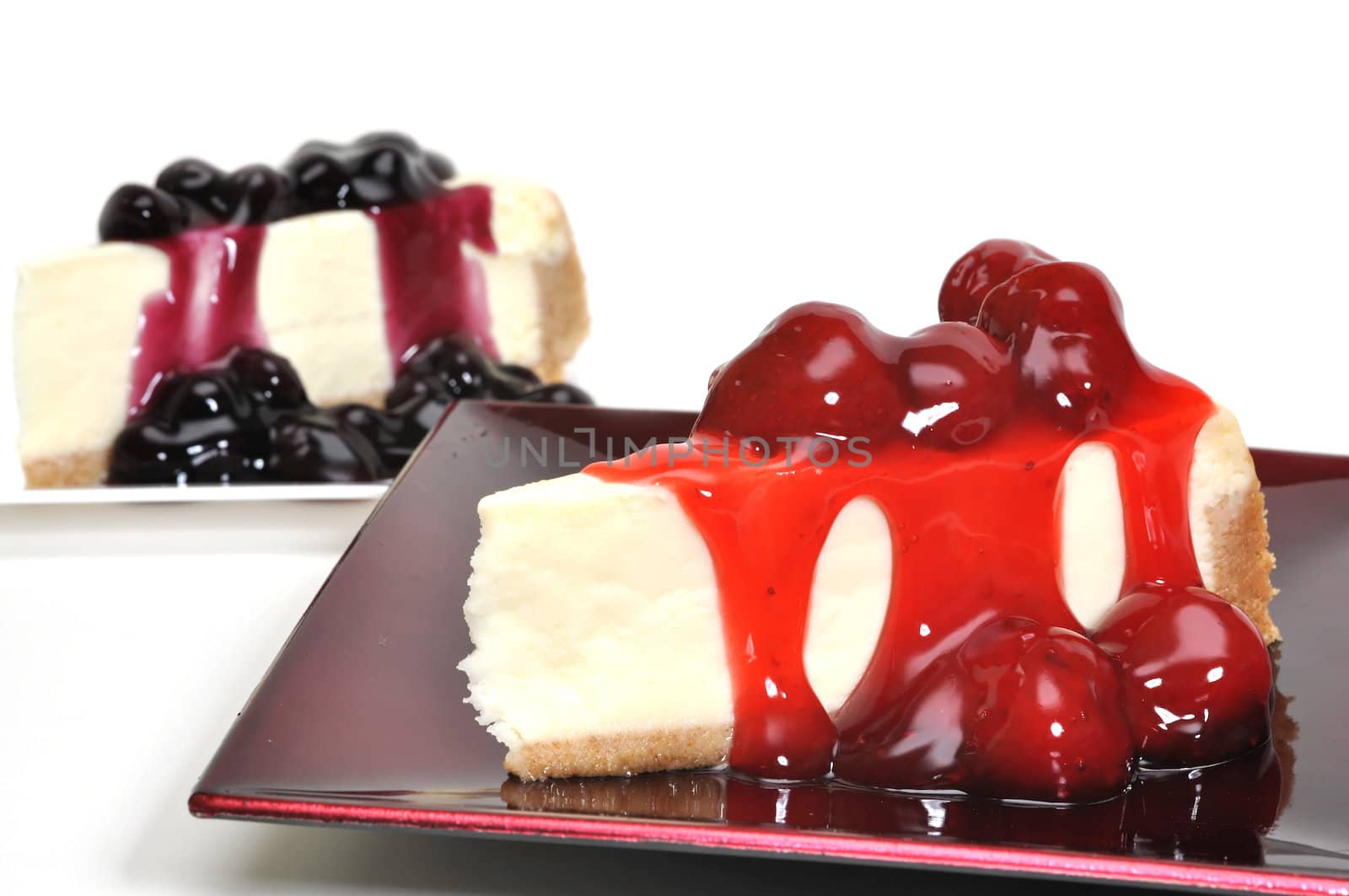 Strawberry and blueberry cheesecake slices isolated on white background.