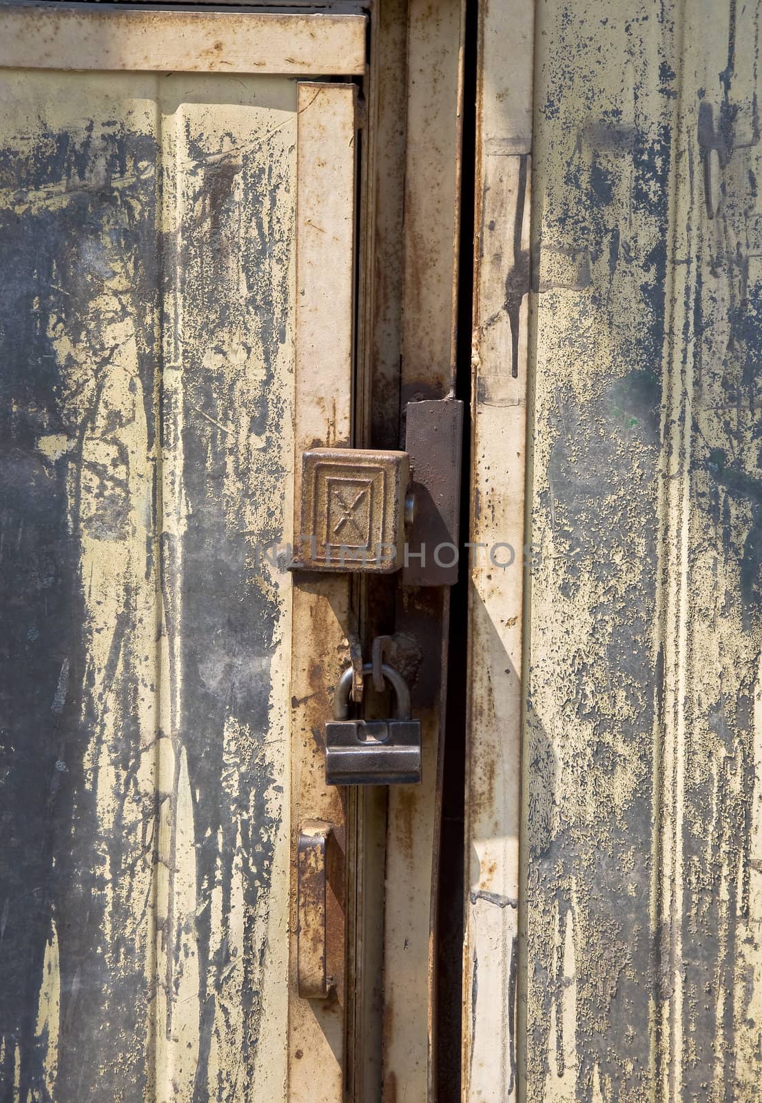 Detail of old door with a bolt. Metal and peeling paint. Padlock.