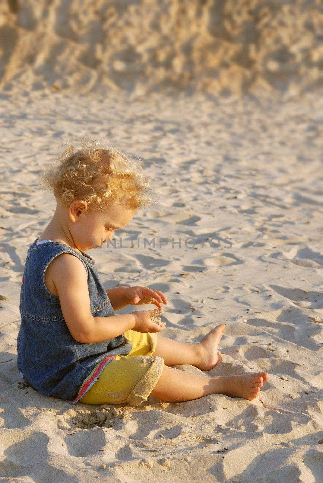Little girl playing on the beach with sand. A boy in his back out of focus in the background.