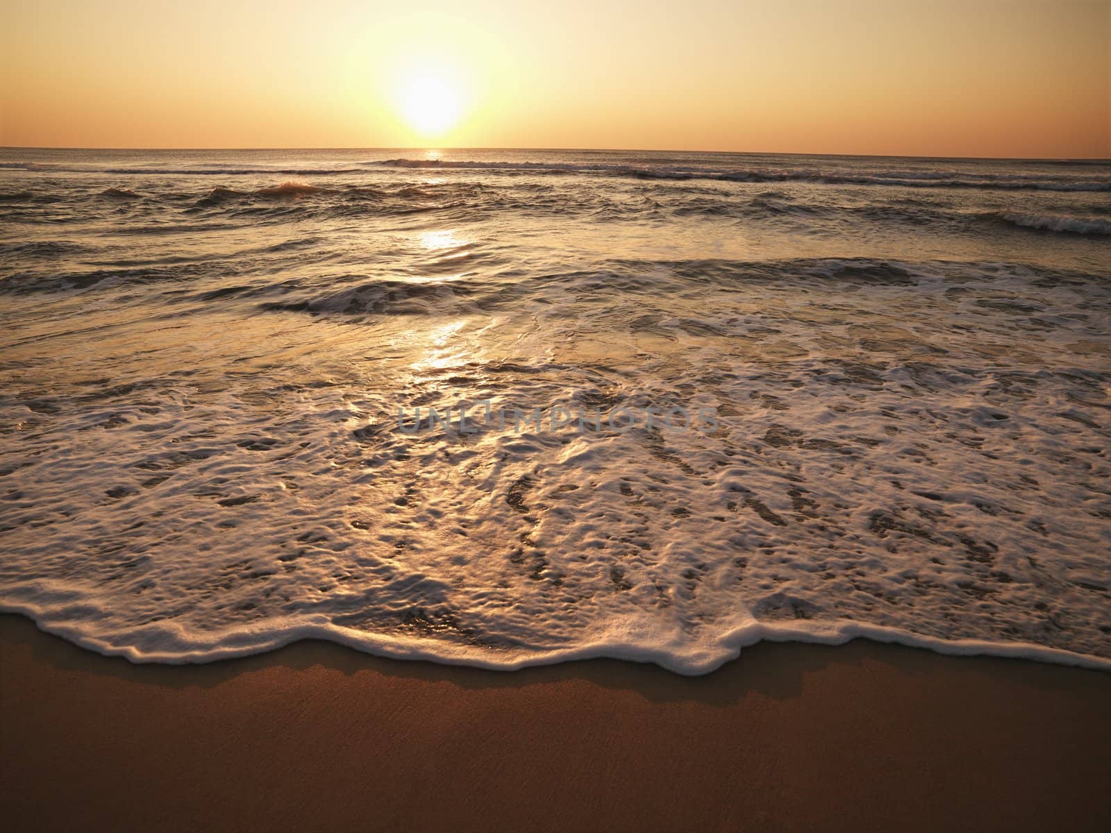 Crashing waves with sun setting on horizon in background.