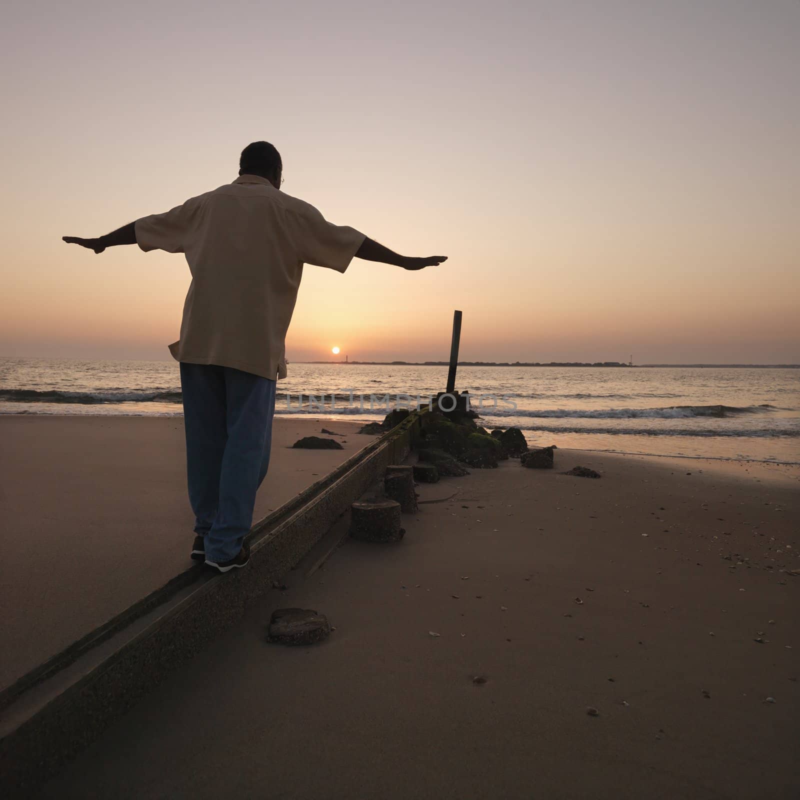African American male balancing on beach erosion barrier at beach during sunset