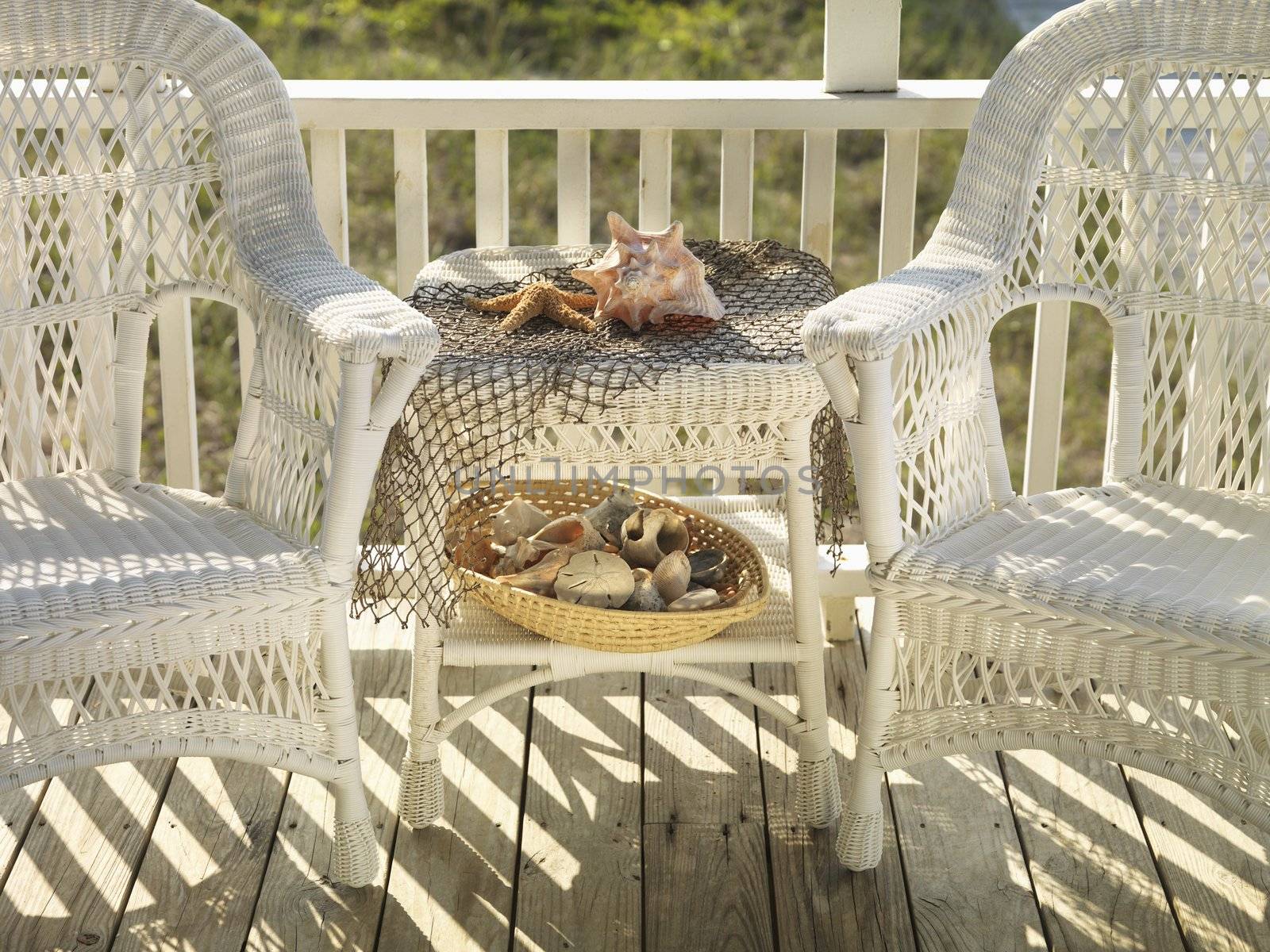 Two wicker chairs with table between them with seashells.