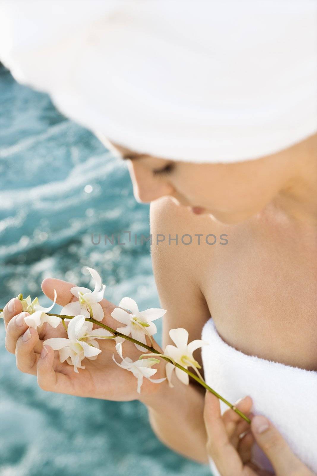 Pretty Caucasian mid-adult woman wearing towel on head holding flowers beside pool.