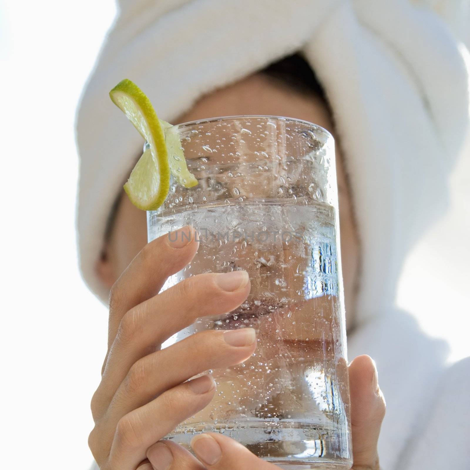 Caucasian mid-adult woman with towel on head holding drink glass with lime slice in front of face.