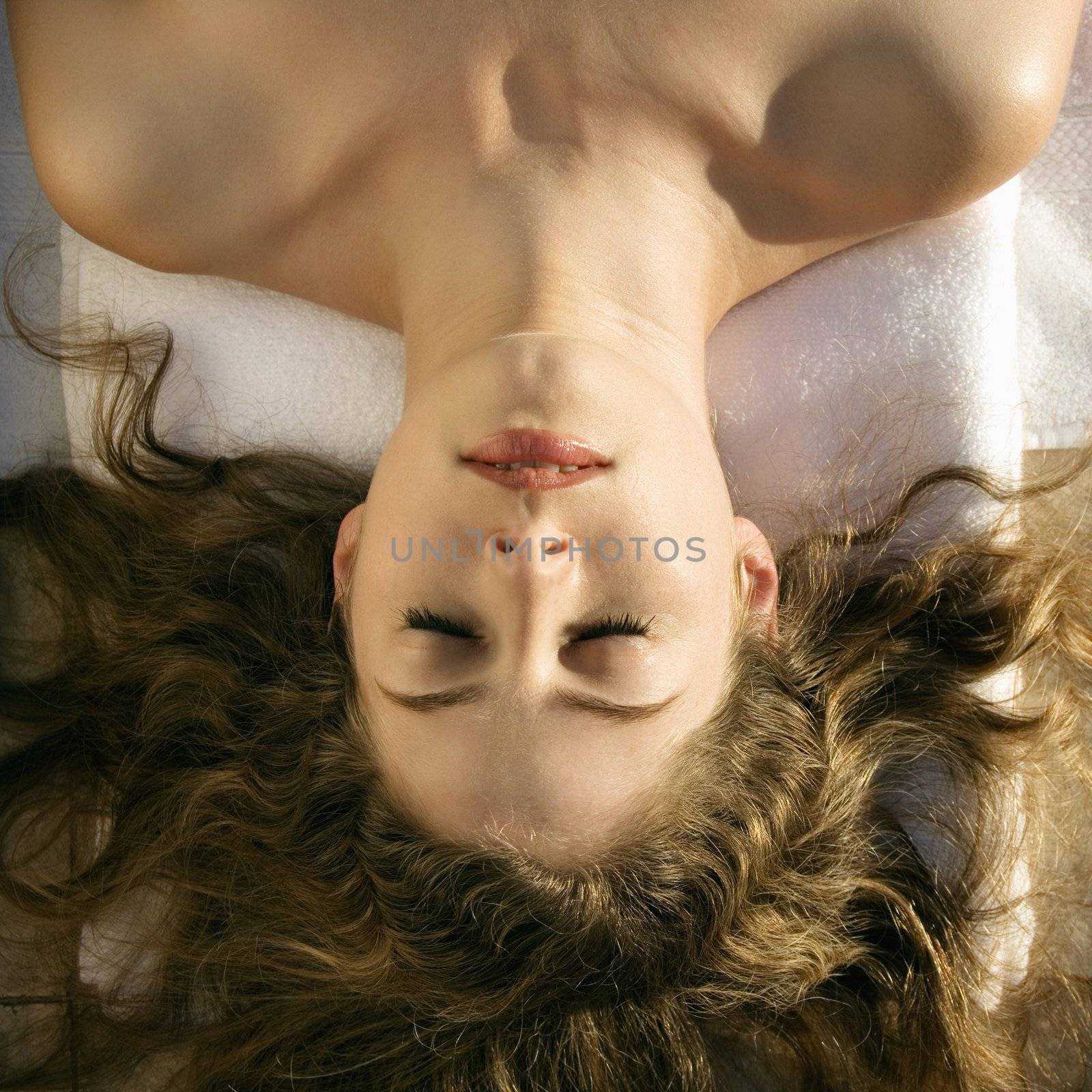Above view of bare Caucasian mid-adult woman lying down with eyes closed and hair spread out.